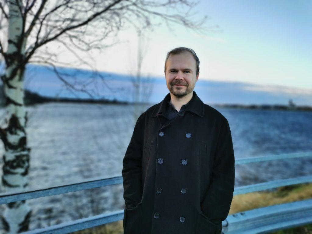 Tomi Bergström seisoo sillalla talvisäässä. Taustalla järvi ja koivupuu.