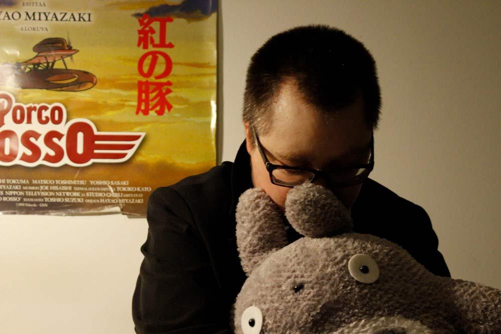 mies istuu ja halaa Totoro-pehmolelua