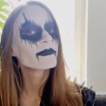 Black metal maskeissa oleva henkilö lähikuvassa ja katsoo hieman hymyillen kameraan